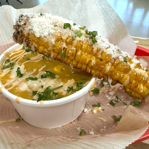 Grilled corn on the cob with parmesan cheese and cilantro, next to a cup of corn chowder.
