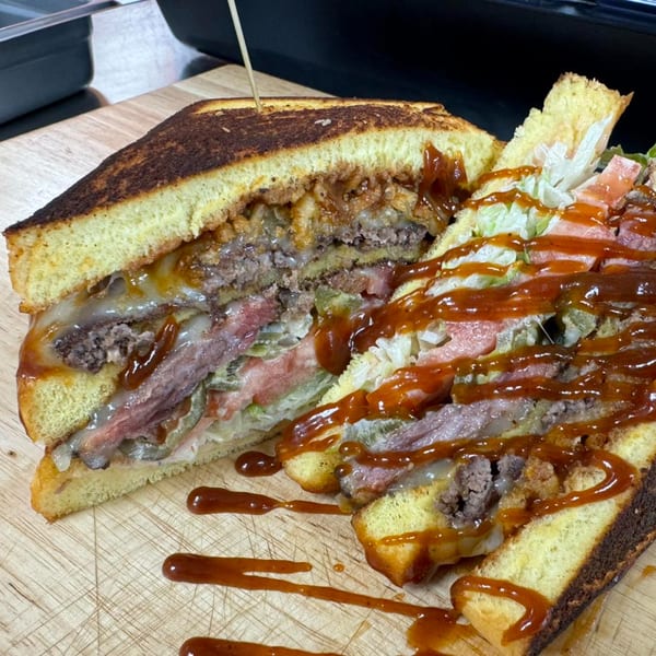 A large, sliced Surf Dawgs Grill sandwich with multiple layers of meat, cheese, and vegetables, drizzled with sauce.