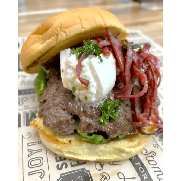 A Surf Dawgs Grill burger with a beef patty, white cheese, red onions, and greens.