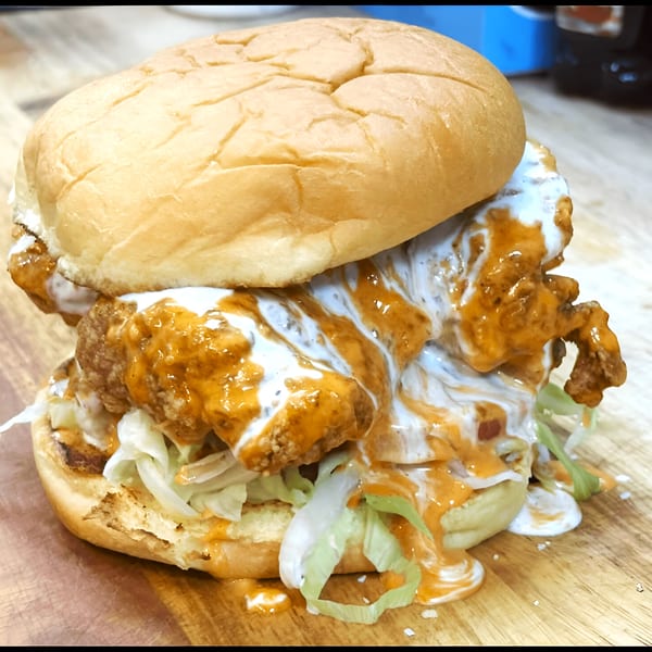 A Surf Dawgs Grill fried chicken sandwich with lettuce and two sauces on a wooden board.