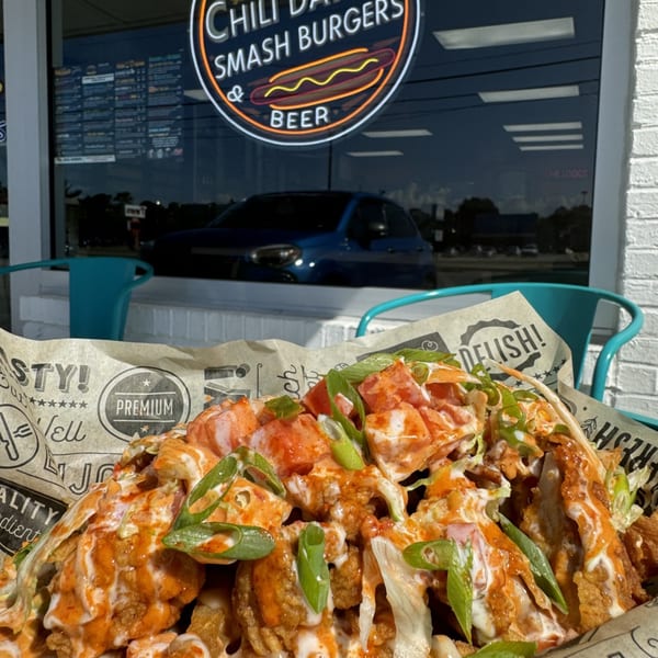 Loaded fries with buffalo chicken, ranch, and green onions, with a restaurant window in the background.