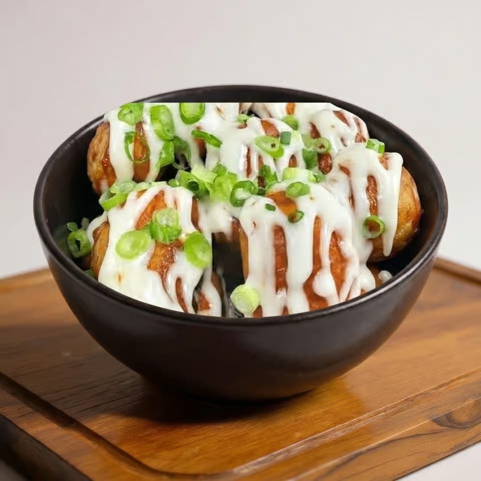Crispy potato wedges topped with creamy white sauce and sliced green onions in a black bowl on a wooden table.