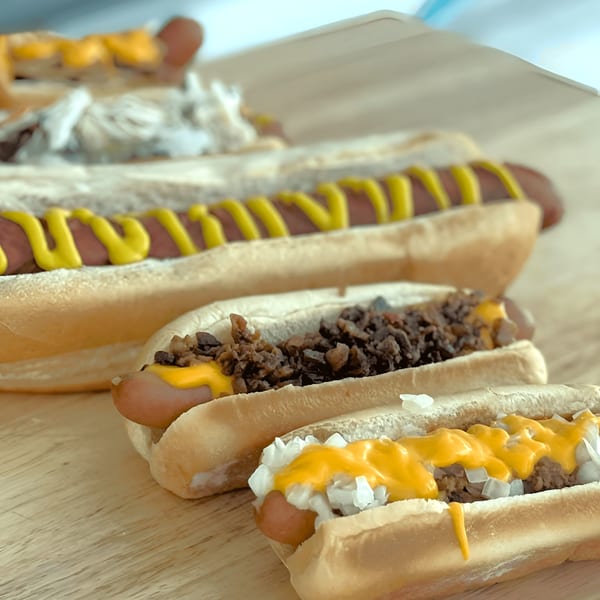 Three Surf Dawgs hot dogs with various toppings, including mustard, chili, onions, and cheese sauce.