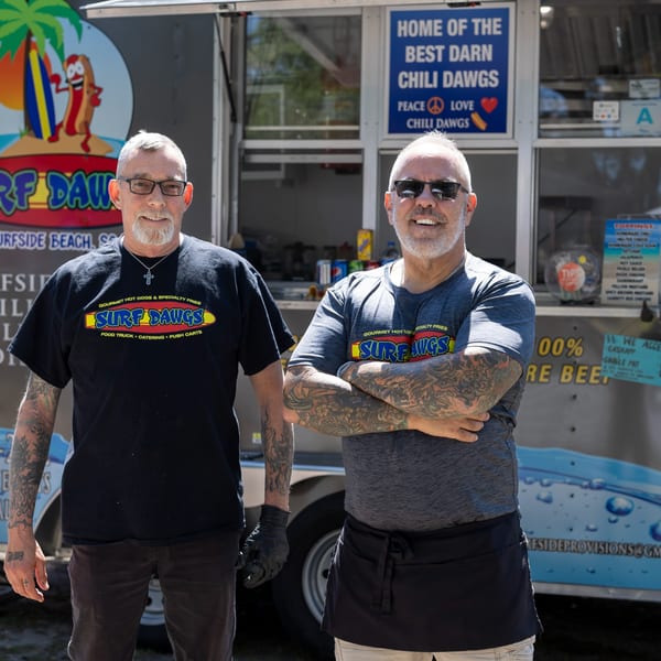 Two men in Surf Dawgs shirts stand proudly in front of their food truck.