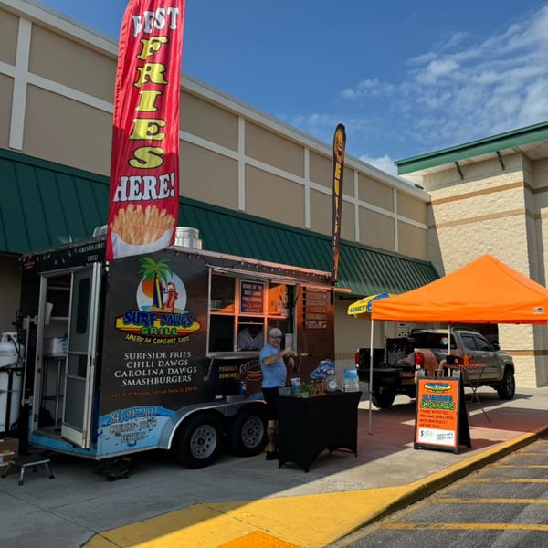 Surf Dawgs Grill food truck with a red "Best Fries Here!" banner and an orange tent.