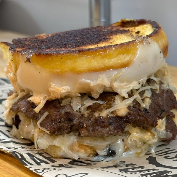 Close-up of a Surf Dawgs Grill burger with melted cheese, sauerkraut, and a toasted bun.